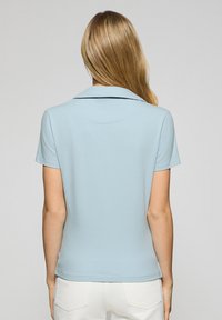 Ljusblå pikétröja med krage, korta ärmar och en figursydd design. Slät textur, minimalistisk stil utan synliga mönster eller detaljer.