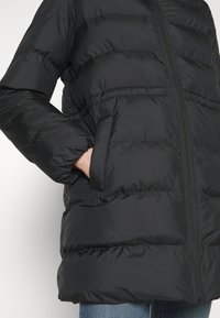 Černá péřová bunda s horizontálním prošíváním, předním zipem a bočními kapsami. Materiál vypadá leskle a je zateplený pro teplo.