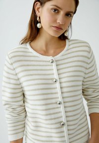 Striped cardigan in cream and beige with a round neck, silver-tone buttons, and textured fabric with contrasting trim along the edge.