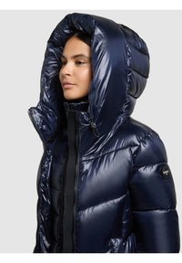 Tamsiai mėlynas pūkinis paltas su puriu, blizgiu paviršiumi, dideliu gobtuvu, užtrauktuku ir šoniniu logotipo lopu. Susiūtos sekcijos suteikia papildomą izoliaciją.