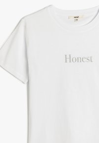 Hvid bomulds T-shirt med korte ærmer og rund halsudskæring. Har ordet "Honest" i sølvmetallic bogstaver på tværs af brystet.