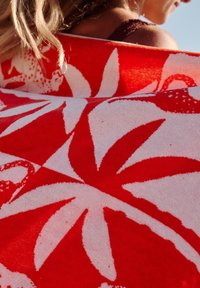 Serviette de plage en coton arborant un motif floral rouge et blanc audacieux, avec une surface texturée et un design vibrant et contrasté.