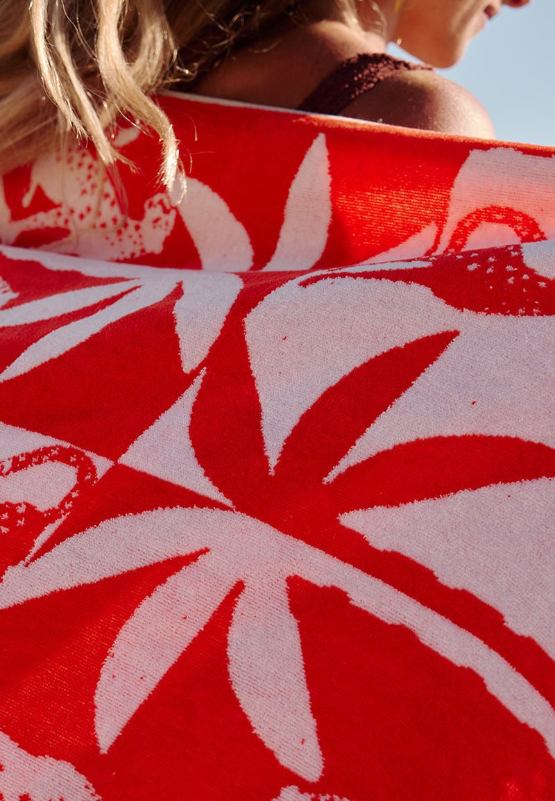 Serviette de plage en coton arborant un motif floral rouge et blanc audacieux, avec une surface texturée et un design vibrant et contrasté.