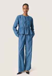 Denimoutfit med en peplumtop med rund halsringning, knytning i framkant och vida byxor. Båda delarna är ljusblå.