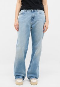 Vaqueros de mezclilla azul claro con un ajuste relajado, que presentan un diseño clásico de cinco bolsillos, textura desgastada y costuras decorativas.