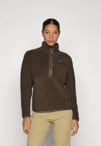 Chaqueta de pullover de forro polar marrón con un alto cuello, cremallera media en la parte delantera, un bolsillo con cremallera en el pecho y dos bolsillos laterales. Superficie exterior texturizada.