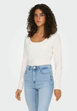 Langmouw, scoop-neck top in het wit, gecombineerd met hooggesneden lichtblauwe jeans met een klassieke knoop- en ritssluiting.