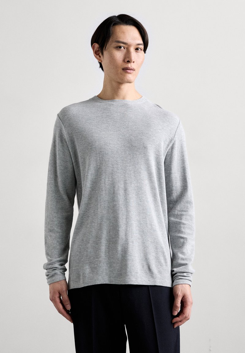Hellgraues langärmeliges T-Shirt mit Rundhalsausschnitt aus weichem Material, mit lockerer Passform und gerippten Bündchen, kombiniert mit dunklen Hosen.
