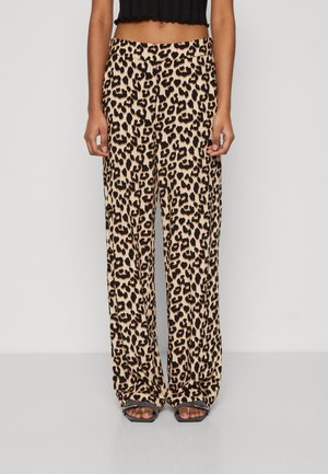 Femme portant un pantalon taille haute à jambes larges avec un imprimé léopard beige et noir, assorti à des sandales noires à bout ouvert et un top noir court.