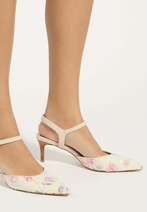 Feet wearing beige slingback heels with thin straps and pointed toes, featuring a subtle floral pattern in pink and light blue.