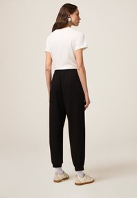 Weißes T-Shirt mit kurzen Ärmeln, kombiniert mit locker sitzenden schwarzen Hosen und beigen Sneakern. Die Hosen haben einen elastischen Bund und gekrempelte Knöchel.