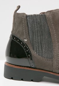 Bottine en daim gris avec talon noir brillant, panneau latéral élastique et semelle noire robuste sur fond blanc.