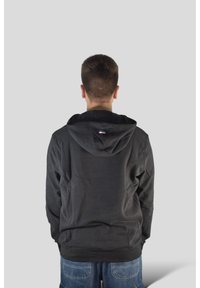 Czarna bluza z kapturem o luźnym kroju, z metką z logo z tyłu. Do tego niebieskie krótkie spodenki dżinsowe o gładkiej fakturze.