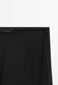 Jupe noire élégante avec fermeture à glissière latérale, détails de coutures discrètes et ceinture, photographiée sur un fond blanc uni.