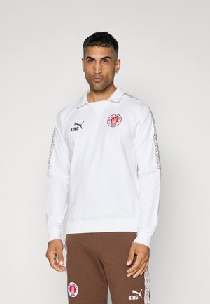 Hvid langærmet polo-shirt med krave, der har et cirkulært logo, brune accenter og mønstrede striber langs ærmerne.