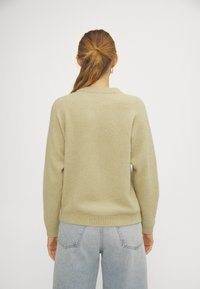 Ljusbeige tröja med mjuk textur, med rundad halsringning och ribbade ärmslut. Matchas med ljusblå högmidjade jeans.