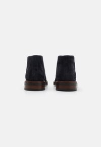 Nabuk čizme do gležnja u tamnoplavoj boji s glatkom teksturom, s drvenom potplatom i zaobljenim vrhom, dizajnirane za izdržljivost i udobnost.