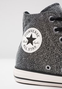 Schwarze und silberne Glitzer-High-Top-Sneaker mit einer weißen Gummisohle, die ein rundes Logo-Patch an der Seite und schwarze Schnürsenkel aufweist.