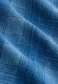 Modrý kostkovaný materiál s měkkým, strukturovaným povrchem. Vzor obsahuje jemný gradient, který ukazuje různé odstíny modré.