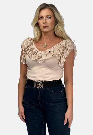 Nagi top z falbanami i głębokim dekoltem w kształcie V, zestawiony z ciemnymi dżinsami i czarnym paskiem z metalową klamrą. Gładka tekstura, elegancki design.