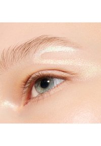 Gros plan sur un œil à la peau claire, avec des cils foncés et un léger reflet scintillant au-dessus du sourcil. Iris bleu-vert.