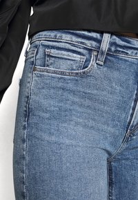 Jeans de denim azul claro con una forma ajustada, que cuentan con un pequeño bolsillo delantero, bolsillos traseros estándar y detalles de costura visibles.