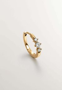Anillo de aro dorado con tres piedras redondas y transparentes engastadas en garras. Superficie suave con un acabado pulido, que muestra un diseño curvado y simple.