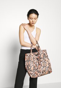 Sac cabas à imprimé léopard dans des nuances de brun, orange et noir ; fabriqué en tissu avec deux poignées. Forme carrée avec ouverture supérieure.