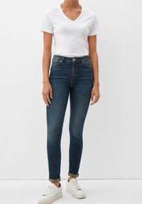 Jeans de tiro alto en azul oscuro con un fit ajustado, con puños enrollados. Combinados con una camiseta blanca de manga corta con cuello en V y zapatillas blancas.