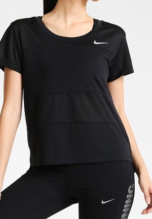 Osoba nosząca czarną sportową koszulkę Nike z krótkim rękawem oraz czarne legginsy z logo Nike i wzorzysty panel boczny.