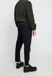 Donkergroene trui met een fluweelachtige textuur en een losse pasvorm; gecombineerd met zwarte taps toelopende broek; zwarte sneakers met een gestructureerd bovenwerk.