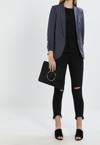 Grå blazer, svart peplumtop, rivna svarta skinny jeans, svarta öppna tå-mules och en svart handväska med ett cirkulärt metalldetalj.