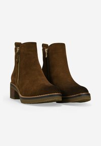 Botines de ante marrón con cremalleras laterales, tacones de bloque y tiradores, mostrados sobre un fondo blanco.