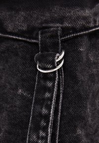 Svart denimväska med rem i silverfärgad metallkoppling, med texturerad yta och synliga sömdetaljer.