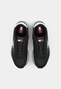 Zwarte sneakers met veters, voorzien van witte en rode accenten. Het ontwerp heeft een gestructureerde bovenzijde en een contrasterende zool. Logo zichtbaar op de tong.