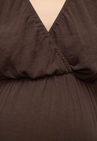 Καφέ υφασμάτινη υφή με σχεδιασμό νουμερώματος V και λεπτομέρεια σύσφιξης στη μέση σε ένδυμα.