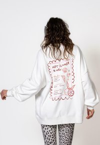 Felpa bianca oversize con grafiche in stile doodle rosse sulla schiena, comprese scritte e illustrazioni giocose di cibo e bevande.