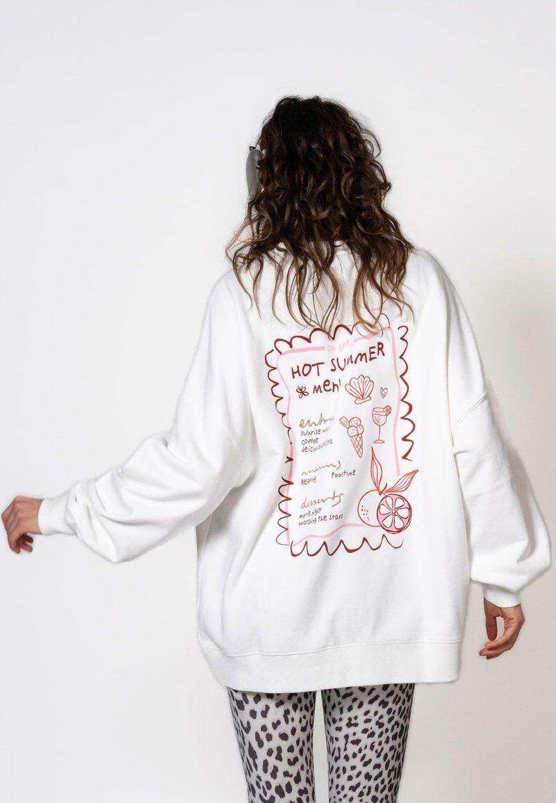 Felpa bianca oversize con grafiche in stile doodle rosse sulla schiena, comprese scritte e illustrazioni giocose di cibo e bevande.