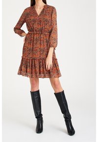 Pitkähihainen, paisley-kuvioinen mekko lämpimissä sävyissä, jossa on empire-vyötärö ja kerroksellinen röyhelöhelma, yhdistettynä polvipituisille mustille saappaille.