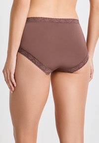 Donna che indossa un perizoma marrone a vita alta con bordo in pizzo, vista di spalle su uno sfondo chiaro e semplice.