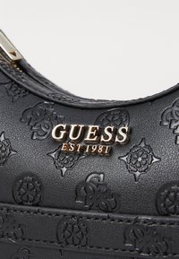 Borsa in pelle nera con motivi impresso, dettagli in logo dorato e finitura testurizzata. Dettaglio della cerniera visibile nella parte superiore.