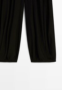 Pantaloni neri dal taglio ampio con polsini elastici raccolti alle caviglie, mostrati su uno sfondo bianco semplice.