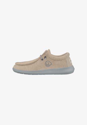 Zapato casual beige tipo slip-on con parte superior de tela suave, suela gris, dos ojales metálicos y logo en el lateral, diseñado para comodidad y uso diario.