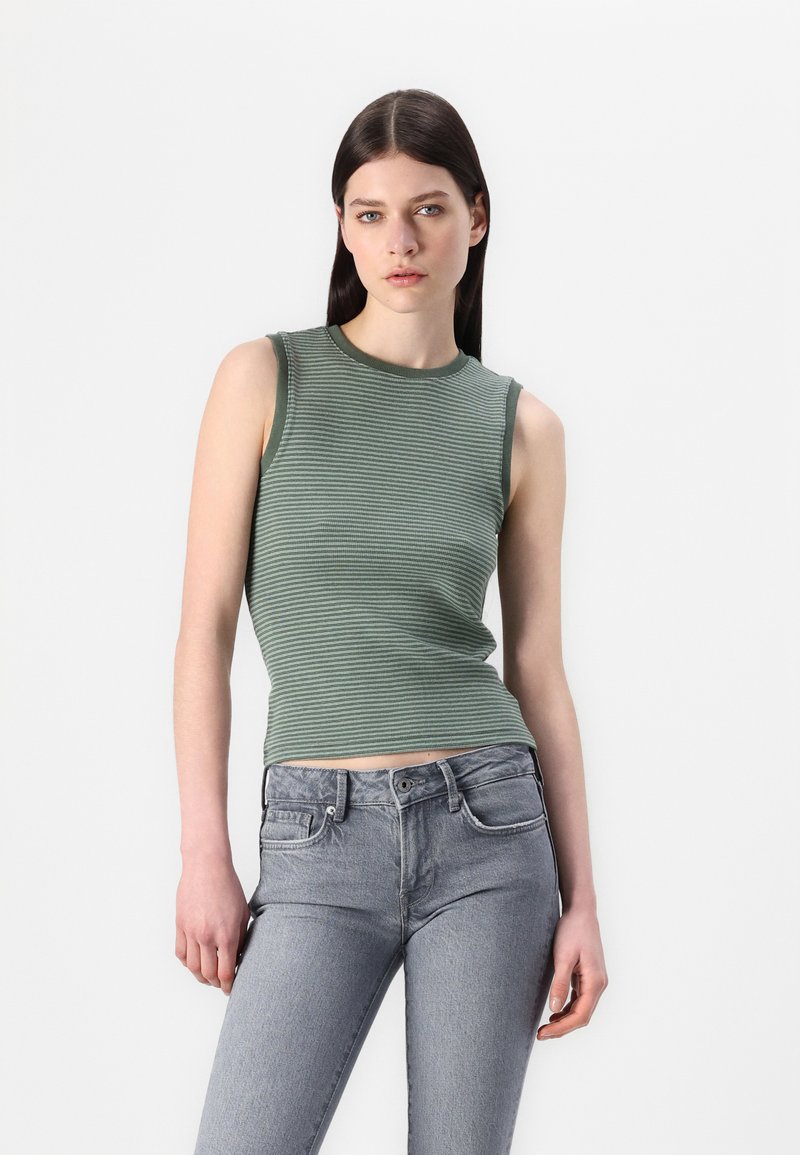 Top senza maniche a righe verdi con texture a costine, scollatura rotonda e design aderente, abbinato a jeans a vita alta grigi chiari.
