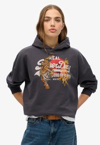 Hoodie gris foncé en coton avec un design de tigre et le logo de la marque sur le devant. Présente une coupe ample et une capuche avec cordon de serrage.