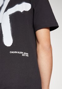 T-shirt in cotone nero Calvin Klein con una grande grafica bianca e il testo del logo "CALVIN KLEIN JEANS EST 1978" nella parte inferiore.