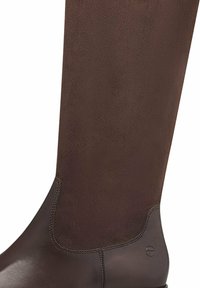 Botte de équitation en cuir marron avec finition lisse et texturée, design ajusté, coutures renforcées et logo subtil à la base.