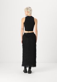 Black sleeveless crop top paired with a black, fringed maxi skirt, featuring a smooth waistband and textured, layered fabric. Chunky black shoes.