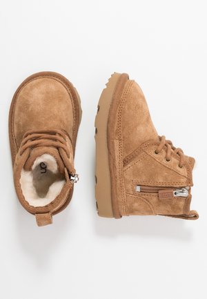 Bottes pour enfants en daim marron avec doublure en fourrure, lacets et fermeture éclair latérale, présentées vues de dessus et de côté sur fond blanc.