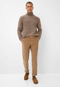Bruine gebreide coltrui met een gestructureerd patroon, gecombineerd met beige corduroy broek en bruine suède schoenen.